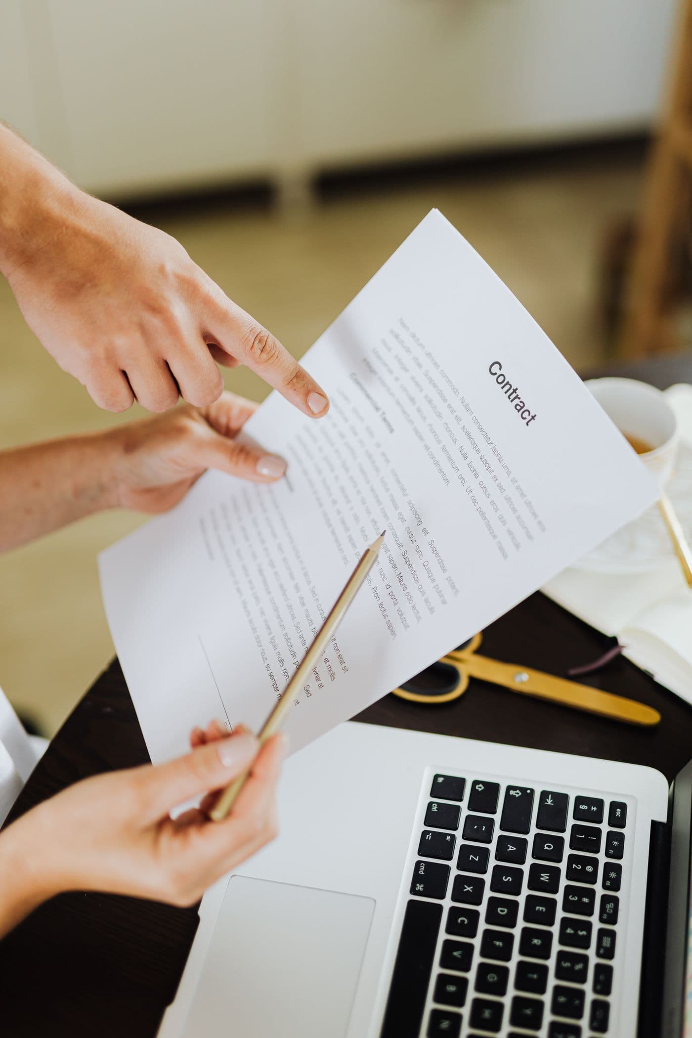 Hands reviewing a contract beside a laptop